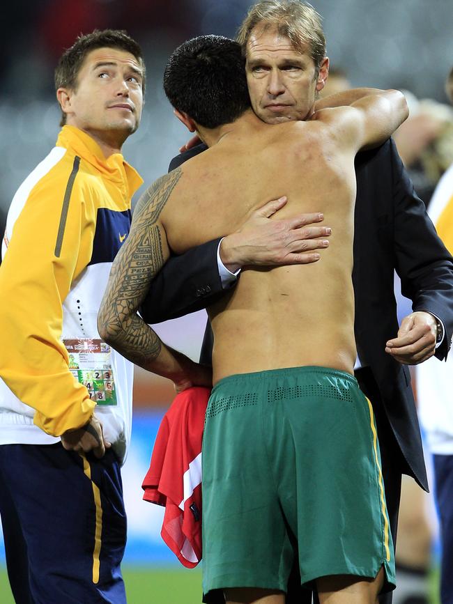 Socceroos player Tim Cahill and Pim Verbeek hug while Harry Kewell, left, watches the TV after Australian exited the 2010 World Cup.