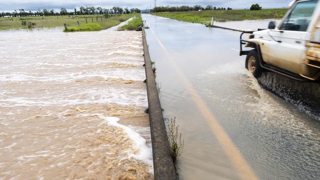 Oakey Creek flows over the Oakey-Cooyar Rd as a motorist navigates flooding in the Oakey area. Picture: Kevin Farmer