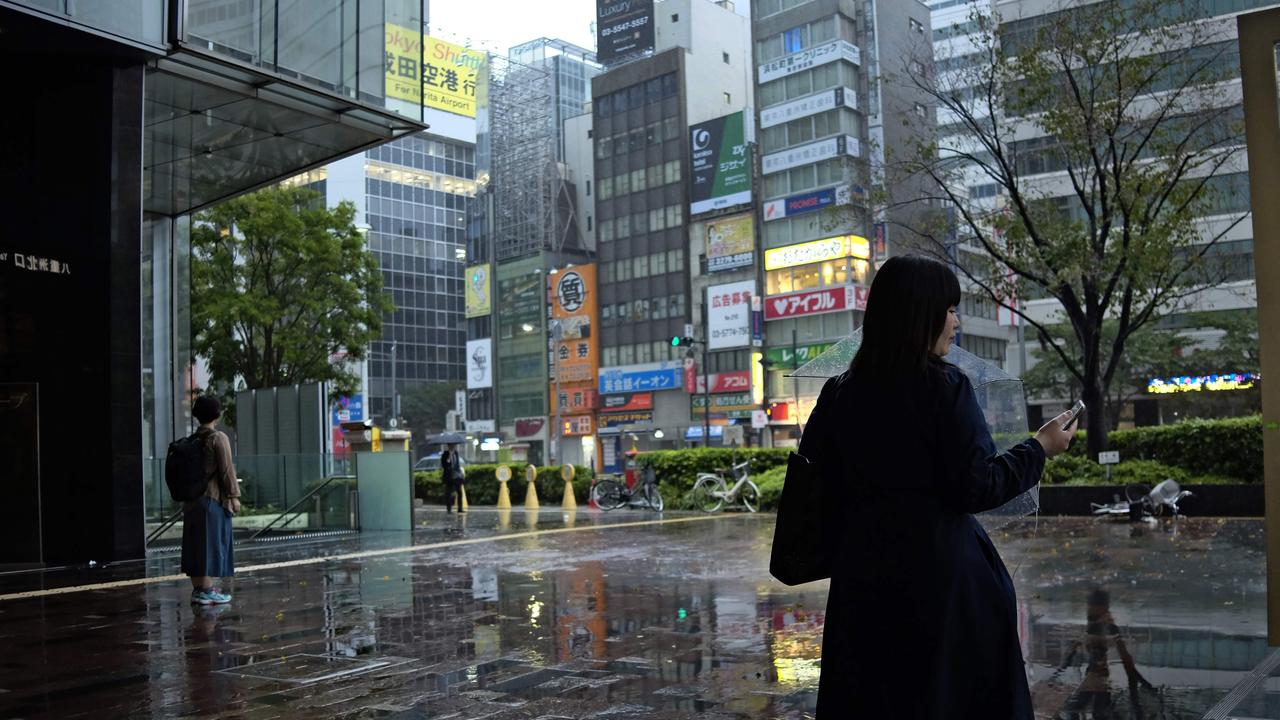 Silent streets: commuters watch the rain at an entrance of the JR Tokyo Station. Picture: AFP