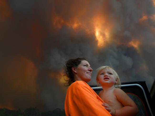 Sharnie Moren and her 18 months old daughter Charlotte look on as thick smoke rises from bushfires near Nana Glen, near Coffs Harbour, Tuesday, November 12, 2019. There are more than 50 fires burning around the state, with about half of those uncontained. (AAP Image/Dan Peled) NO ARCHIVING