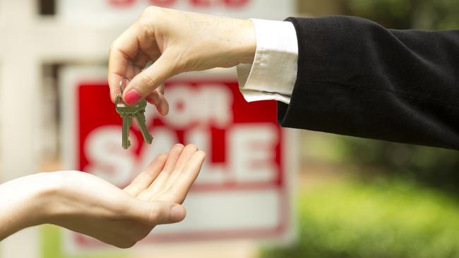 iStock photo of agent handing over keys in front of a for sale / sold sign. For On the Pulse column in Cairns Post weekend real estate liftout.