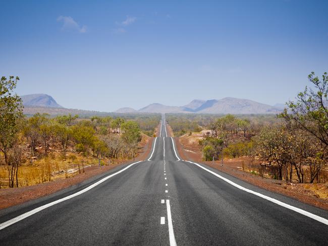 The open road in Kimberly, Western Australia. Straight single lane asphalt road stretching into the distance with mountains in the background. Holiday adventure.