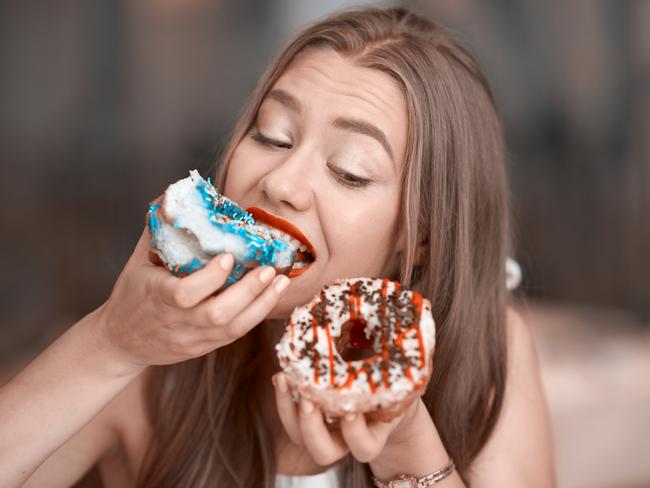 cute young woman holding donuts and biting it.cravinf for sweets.horizontal lifestyle shot. for Cairns Sun food column by Julia Wedding, June 6, 2017