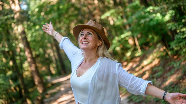 Adult woman with long blond hair and a straw hat, wearing light summer clothes, enjoying summertime in the woods. Middle-aged early retirees generic