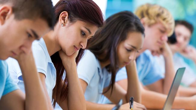 Row of private high school students work on assignment in class. They are writing or using laptops or digital tablets. They are concentrating as they study. They are wearing school uniforms. Picture: iStock