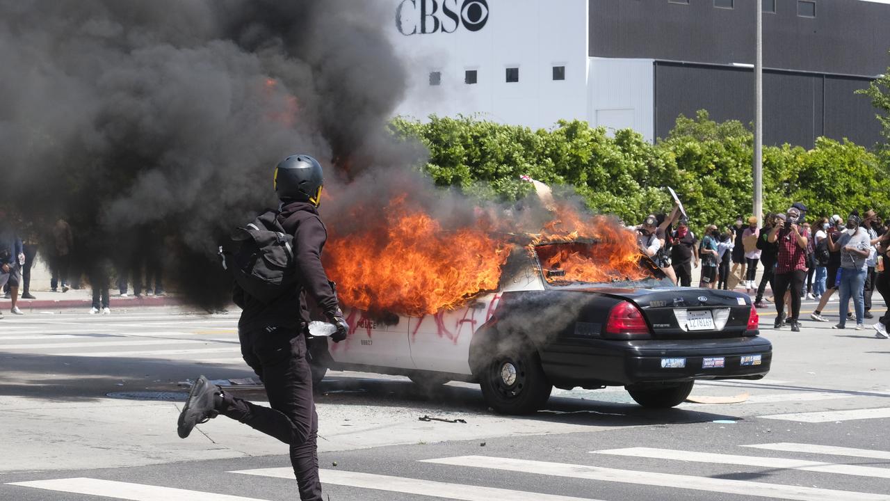 A person runs while a police vehicle is burning during a protest over the death of George Floyd in Los Angeles. Picture: AP Photo/Ringo HW Chiu