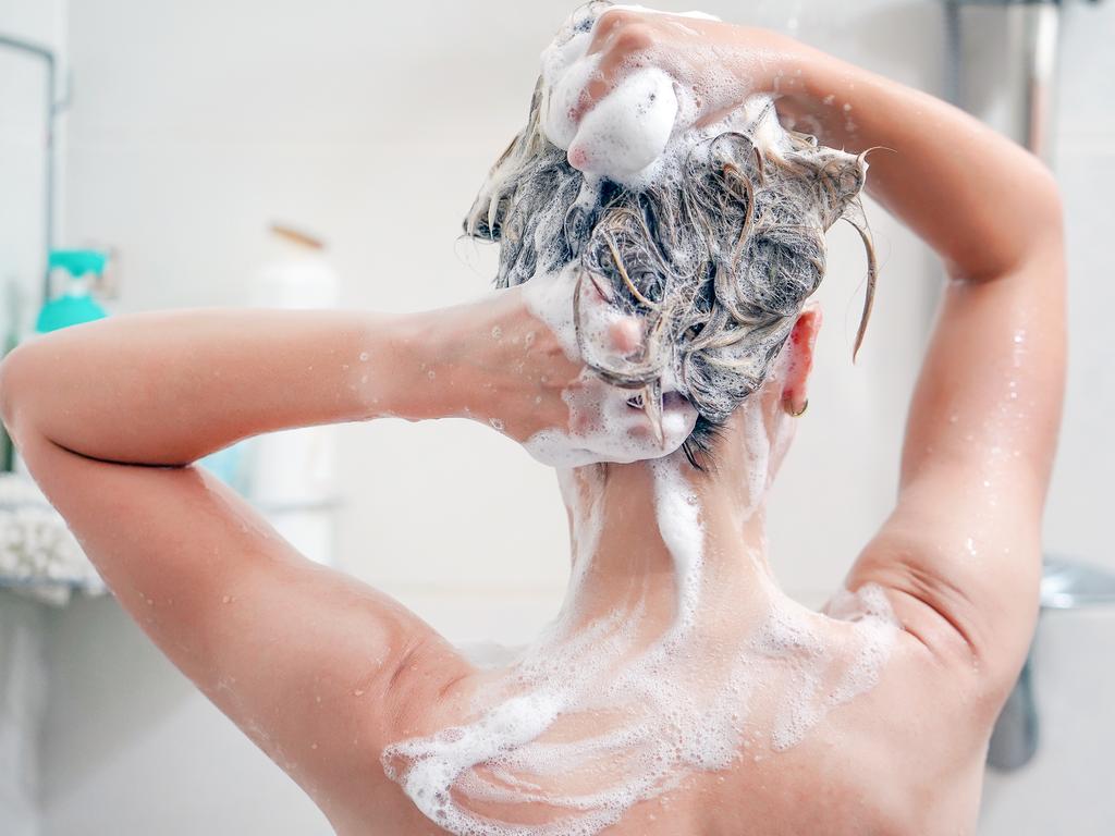 Woman washes her hair with shampoo in bathroom. Woman washing her hair with a lot of foam inside a shower. Back view of young woman washing her hair.