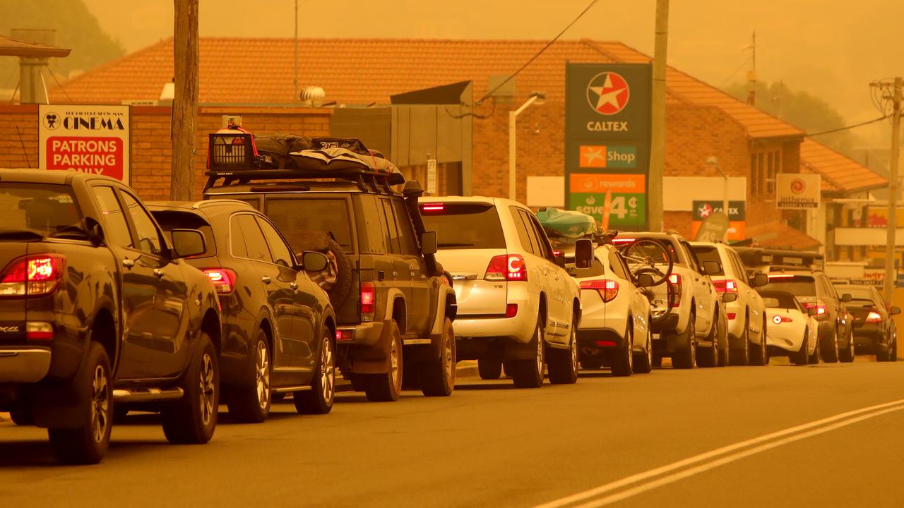 People queue for petrol in the smoke at Merimbula after bushfires cut off the entire south coast of NSW. Picture: Stuart McEvoy