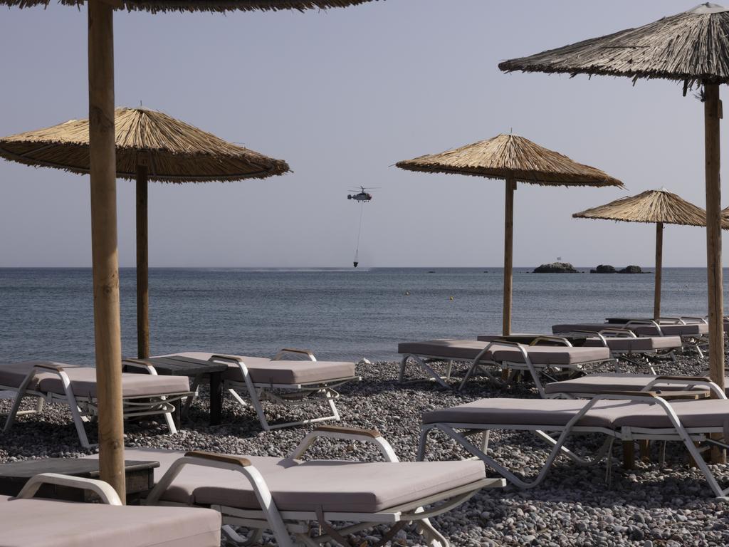 A firefighting helicopter is framed by empty sun lounges as it scoops up water to take to a forest fire in Rhodes, Greece. Picture: Getty Images