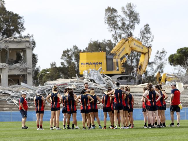 The Crows AFLW team assembles on the old Footy Park, as coach Matthew Clarke addresses them. The once-loved stands are semi-demolished in the background. Picture: Sarah Reed