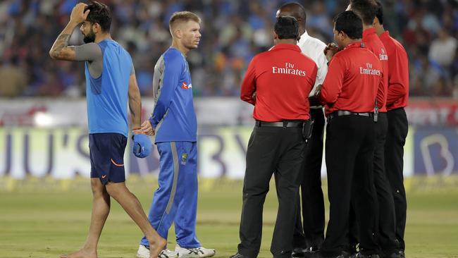 Umpires and match officials talk to Australian cricket captain David Warner, second left, about the condition of the outfield, as Indian cricket captain Virat Kohli walks back, before the start of the third and final Twenty20 cricket match in Hyderabad, India, Friday, Oct. 13, 2017. The match has been delayed because of the wet outfield. (AP Photo/Manish Swarup)