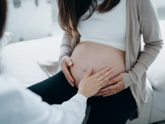 Cropped shot of Asian pregnant woman having a consultation with doctor during routine check up at clinic. Doctor is performing an examination and touching the belly. Check-ups, tests and scans to ensure a healthy pregnancy for both mother and unborn baby