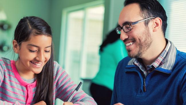 Mid adult Hispanic dad helps his pre-teen daughter with school assignment. They are working at the kitchen table with the kitchen in the background.