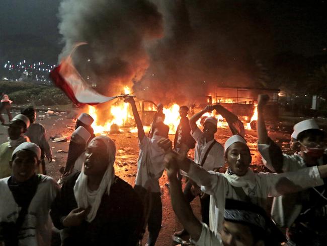 Muslim protesters chant slogans near burning police trucks during a clash outside the presidential palace in Jakarta, Indonesia. Picture: Dita Alangkara.