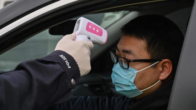 A police officer checks the temperature of a driver on the outskirts of Wuhan, the epicentre of the deadly virus outbreak. Picture: AFP