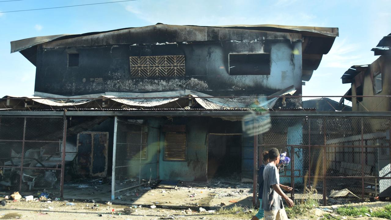 People walk past burnt-out buildings in Honiara's Chinatown on November 27, 2021. Picture: Charley Piringi / AFP