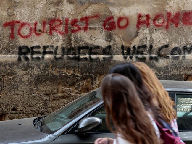 People walk past a graffiti in Palma de Mallorca, in the Spanish island of Mallorca, May 23, 2016. REUTERS/Enrique Calvo - RTX2ERQ3