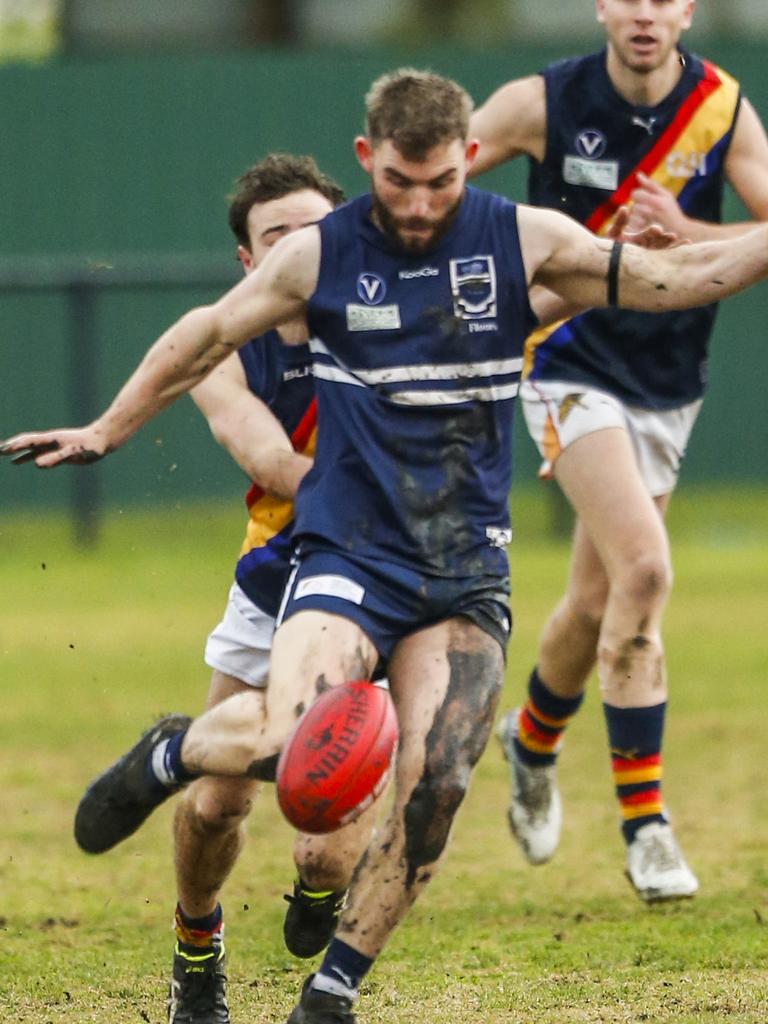 A mud-covered Caulfield Grammarians player boots his team forward in the VAFA. Picture: Valeriu Campan