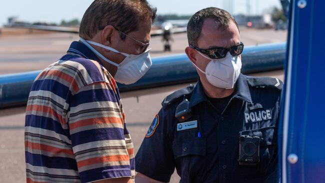 The older of the two men, shoeless and in handcuffs, is placed into the back of a police paddy wagon on the tarmac of Darwin Airport. Picture: Che Chorley