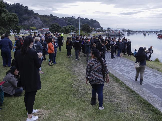 Locals sing during sun rise as they wait for the return of the victims after the White Island eruption to be returned to Whakatane, New Zealand. Picture: AP