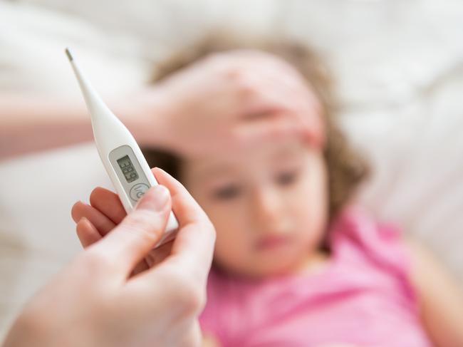 Close-up thermometer. Mother measuring temperature of her ill kid. Sick child with high fever laying in bed and mother holding thermometer. Hand on forehead.