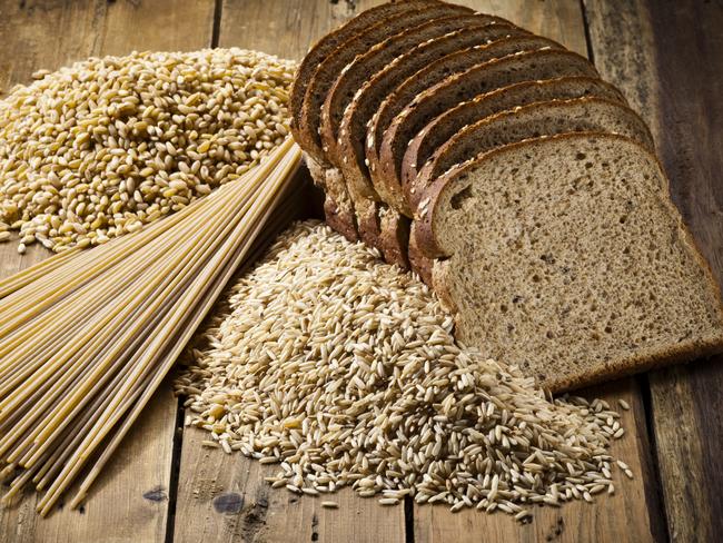 Whole grain bread slices, heap of brown rice and whole grain pasta carefully arranged on rustic wood table. These are whole grain healthy eating food products specially indicated for dieting.