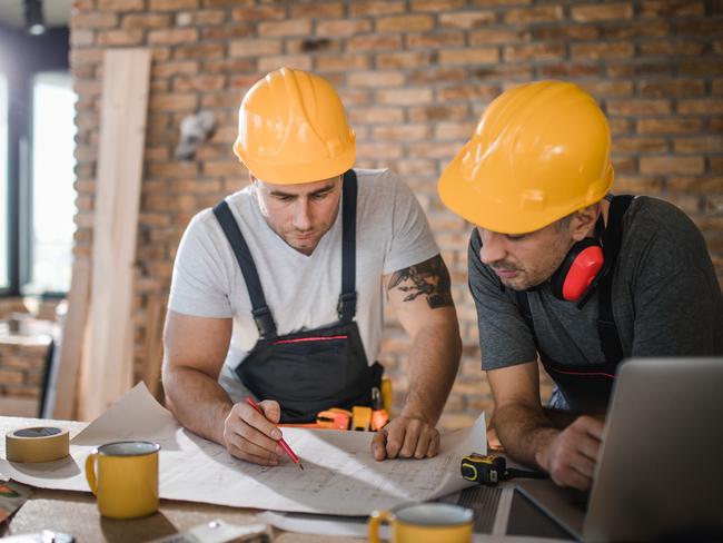 Two mid adult manual workers examining blueprints on construction site.