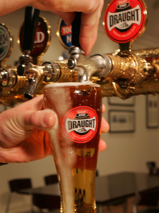 A barman pours a schooner glass of West End Draught beer.