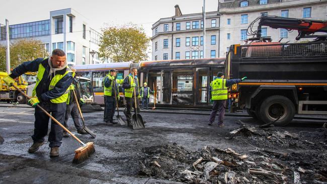 Workers clear the remains of a burnt out bus from a road as a fire-damaged Luas tram stands in the background. Picture: PAUL FAITH / AFP