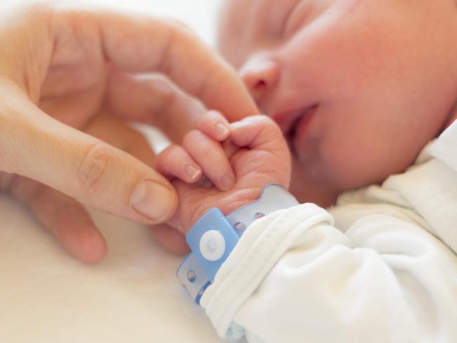 Newborn baby boy sleeping in his crib, his mother's hand holding his little hand.