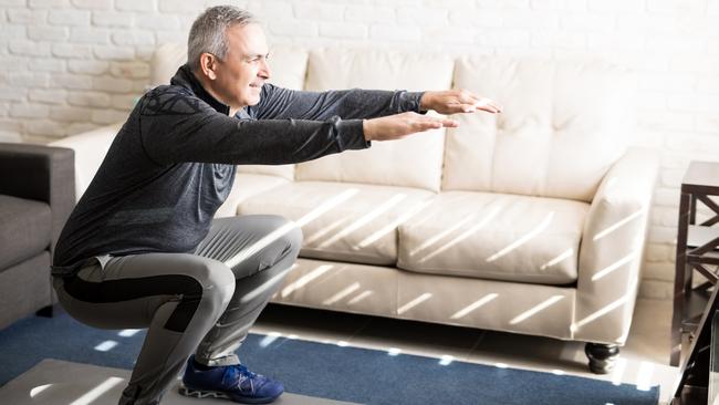 Senior man doing squats and exercising in living room at home