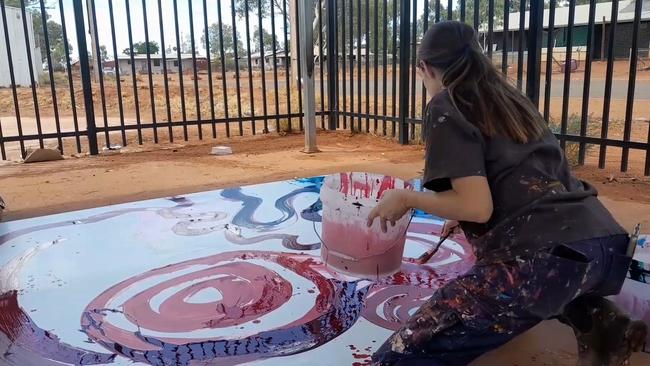 A still taken from video where a non-indigenous employee is seen contributing to a painting by Indigenous artist Yaritji Young.