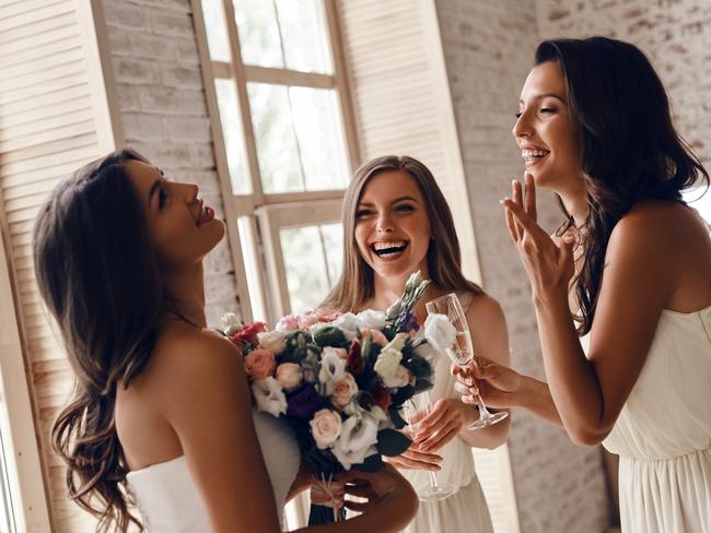 Attractive young woman holding a wedding bouquet and smiling while her girlfriends drinking champagne