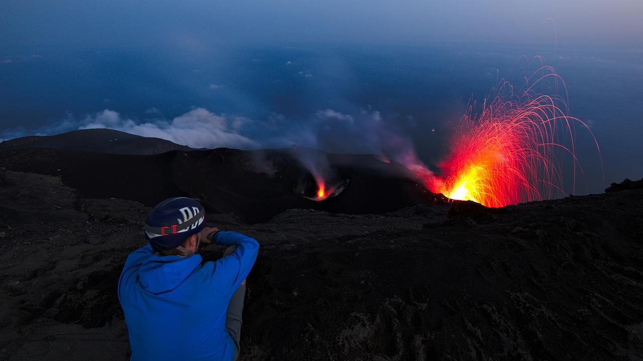 A tourist watching the volcano eruption at night at Stromboli in Italy.