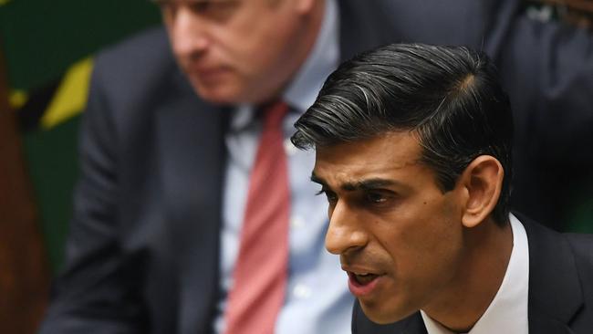 Rishi Sunak speak in the House of Commons with Boris Johnson looking on from behind.