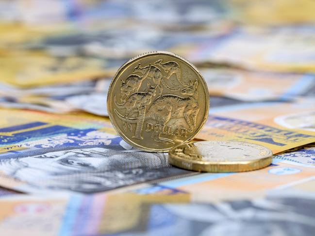 A single Australian One Dollar coin standing on its edge on top of Australian fifty dollar bills; saving money generic