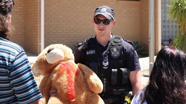 A police officer receives a teddy bear from a member of the public at the memorial for his murdered colleagues.