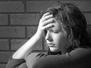 Teenage girl sitting against brick wall with sad facial expression, hand on head, knees bent.