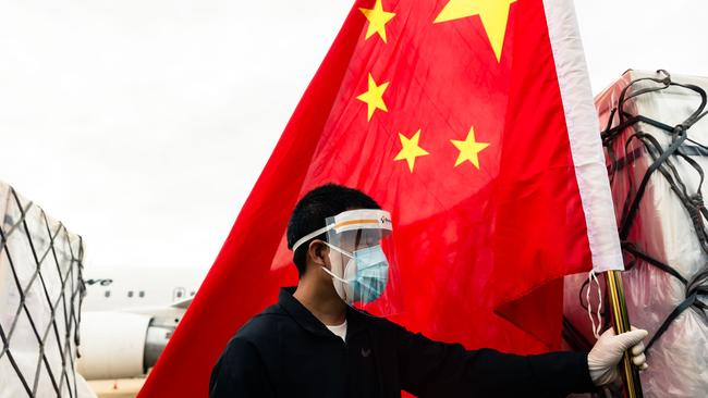 A man holds the Chinese national flagwhile workers offload an Air Zimbabwe aeroplane with a donation of 200,000 doses of the Sinopharm coronavirus vaccine from China last week. Picture: AFP