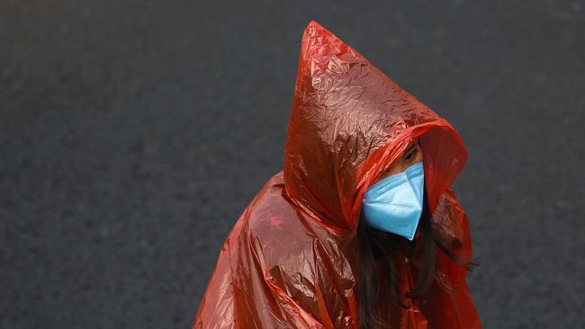 A masked woman in a plastic rain coat walks on a street in Beijing. Picture: AP Photo/Andy Wong