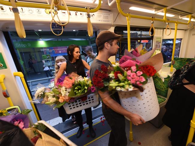 People from the vigil carry floral tributes onto the 86 tram before it goes to Bundoora. Picture: Tony Gough