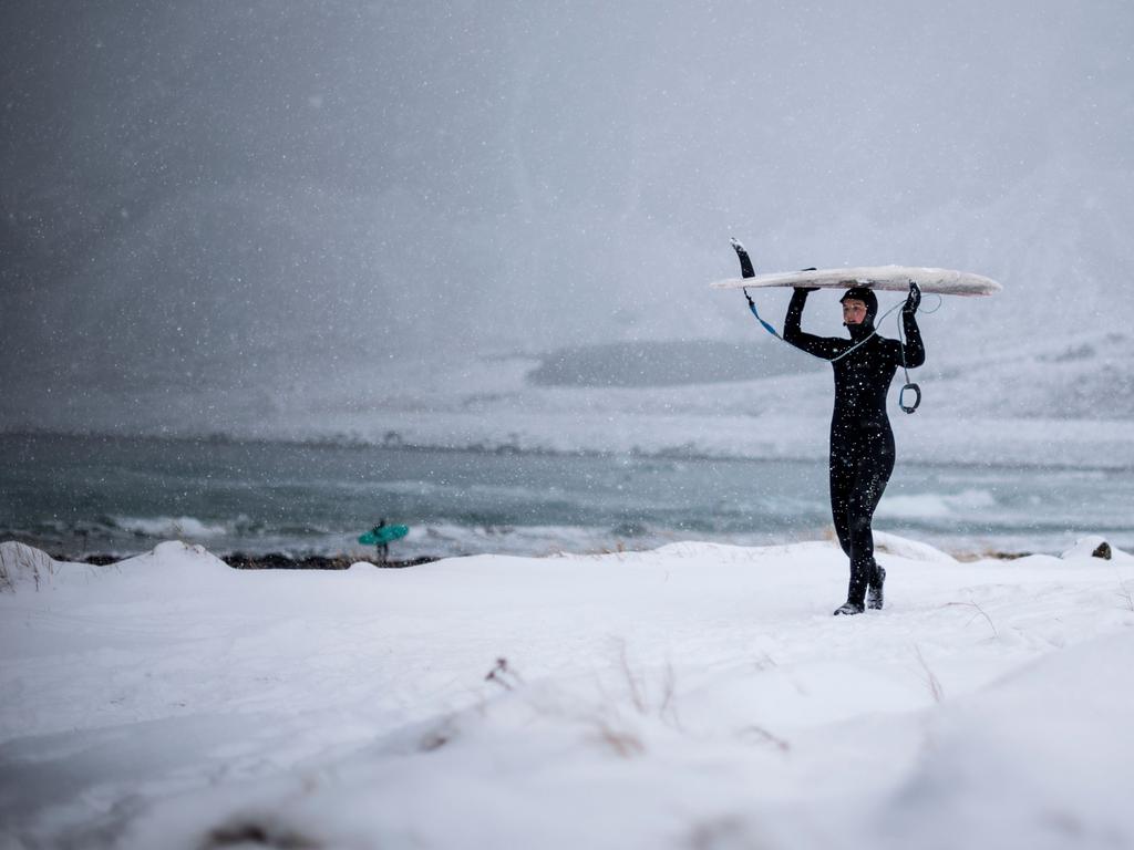 A surfer carries her surfboard as she walks out of the water under snowfall, on March 11, 2018, in Unstad, northern Norway, Lofoten islands, within the Arctic Circle. Picture: AFP