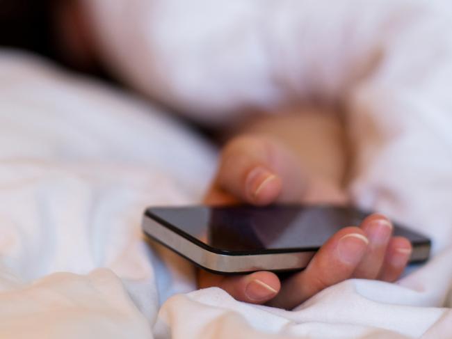 hand holding smartphone when sleeping on bed. Picture: iSTockEscape, sleeping travel wisdom, Natalia Cooper