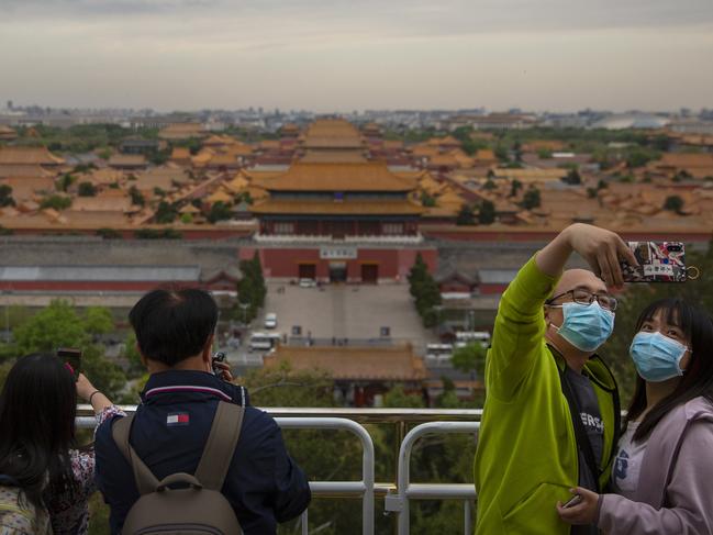 People wearing face masks to protect against the spread of the new coronavirus pose for a selfie at a public park overlooking the Forbidden City.