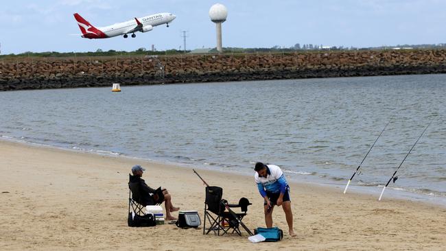 A Qantas plane taking off at Sydney Airport with two fisherman pictured in the foreground. Picture: NCA NewsWire / Damian Shaw