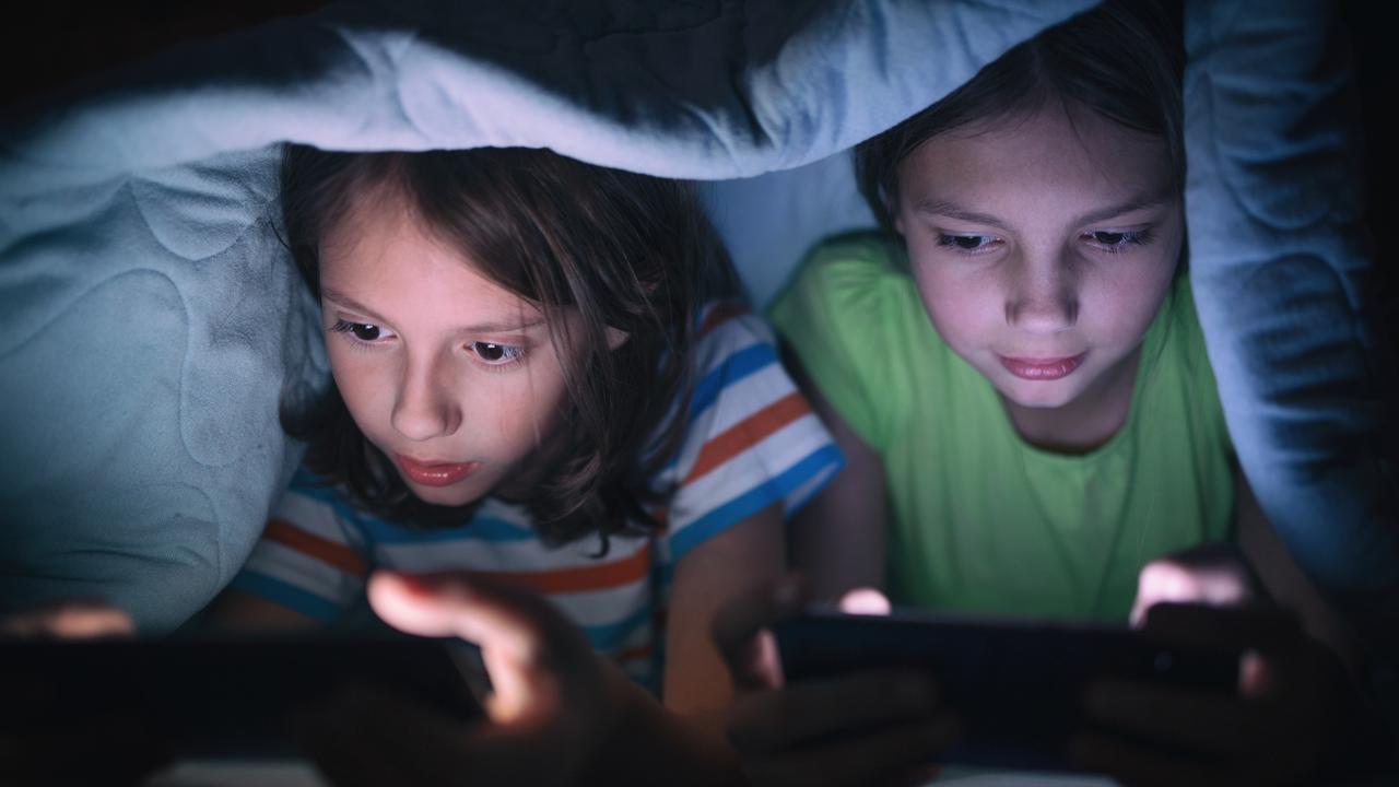 Boy and girl playing games on mobile phones while lying on bed in bedroom under the blanket. They are spending some nice time together that makes them happy.  - picture istock