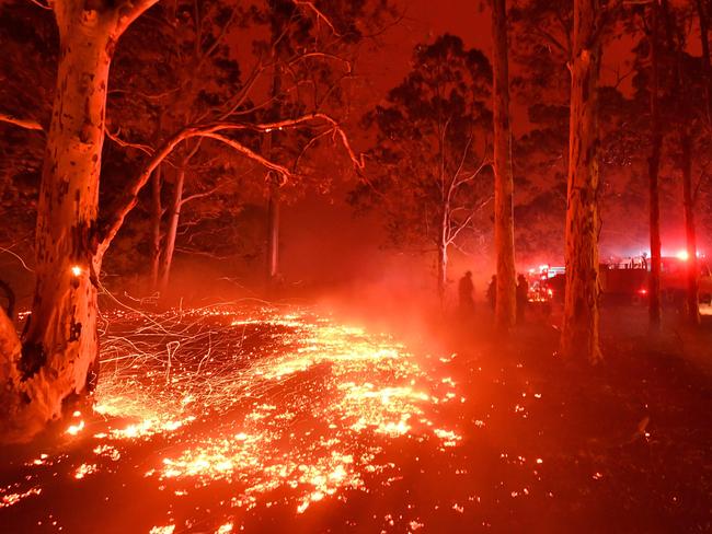Burning embers cover the ground as firefighters (back R) battle against bushfires around the town of Nowra in the Australian state of New South Wales. Picture: Saeed Khan/AFP