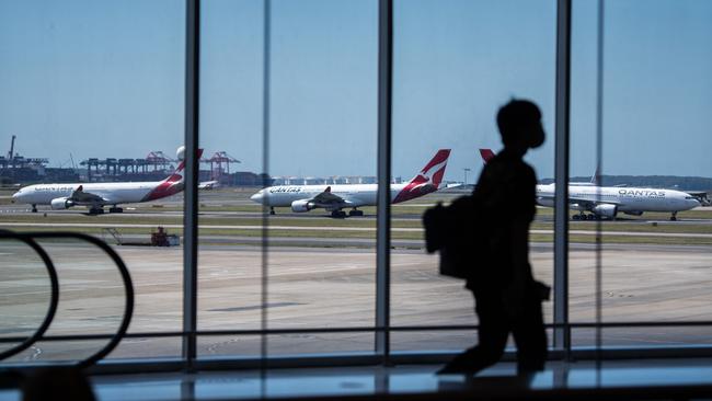 Qantas aircraft on the runway as a passenger passes through the terminal at Sydney International Airport. Picture: NCA NewsWire / James Gourley