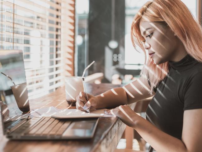 A pretty young focused professional asian woman writing down notes or making a draft. Office worker, businesswoman or freelancer at a coffee shop.