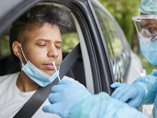 Doctor taking coronavirus sample from male patient's nose. Healthcare workers are in protective workwear. They are standing by car during epidemic.